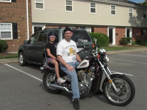 1986 Honda Shadow Aero - A man and a child sit on a burgundy and white 1986 Honda Shadow Aero motorcycle parked in front of an apartment building.