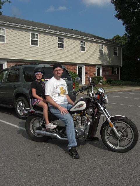 1986 Honda Shadow Aero - A man and a child sit on a motorcycle in front of a building and an SUV.