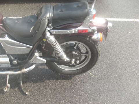 1986 Honda Shadow Aero - The rear section of a motorcycle is shown, a worn seat and a spoked wheel.
