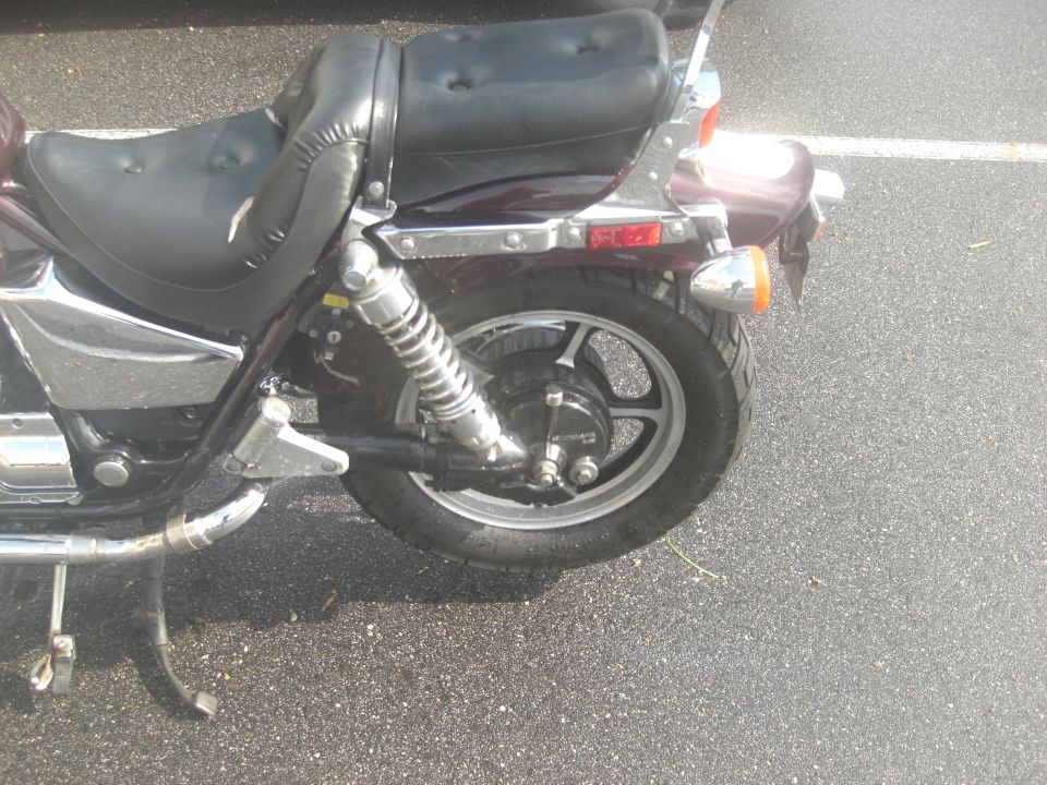 Close-up of a motorcycle's rear wheel, shock, and torn seat