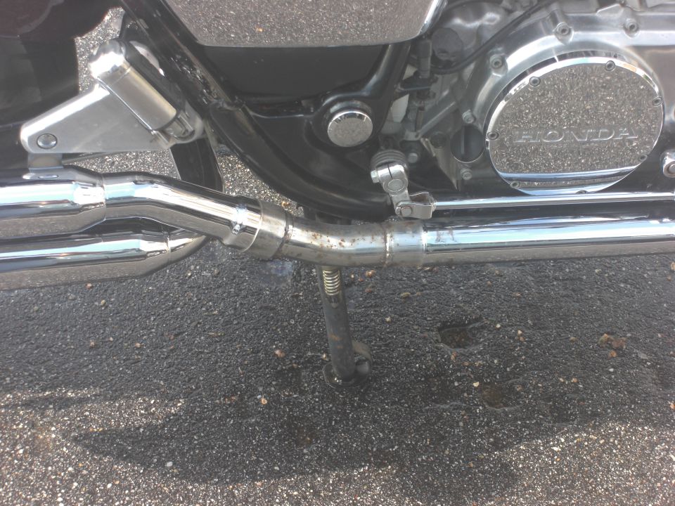 Close-up of motorcycle engine with HONDA logo on cover, chrome exhaust pipes, and kickstand