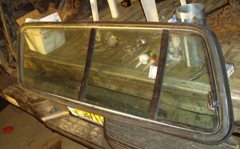 1979 Ford Bronco - Truck cap window assembly with tinted glass and metal frame, seen in a workshop setting.