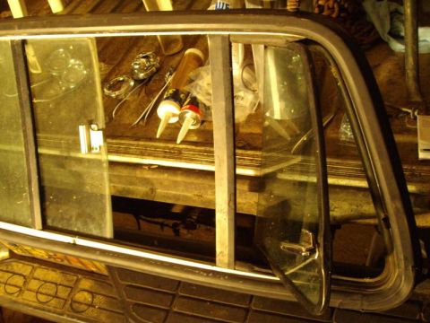 1979 Ford Bronco - A close-up view of a car's window frame and surrounding parts, with tools and supplies visible on a workbench.