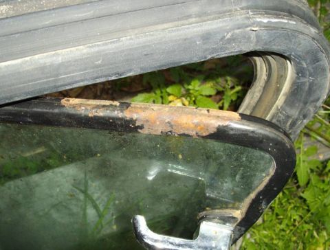 1979 Ford Bronco - Close-up of a rusted window frame with a black rubber seal and glass, showing signs of wear and tear.