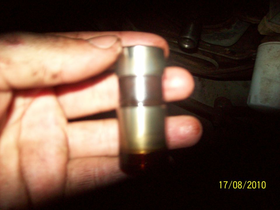 Hand holding a metal engine lifter with oil residue