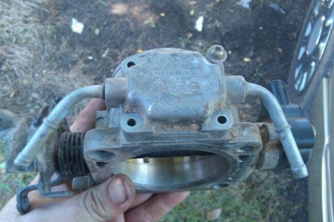 2000 Mercury Grand Marquis - A throttle body part is held in a hand, showing hoses and some stamped text.