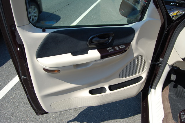 Car door panel with beige and dark fabric, wood trim, and speaker grille