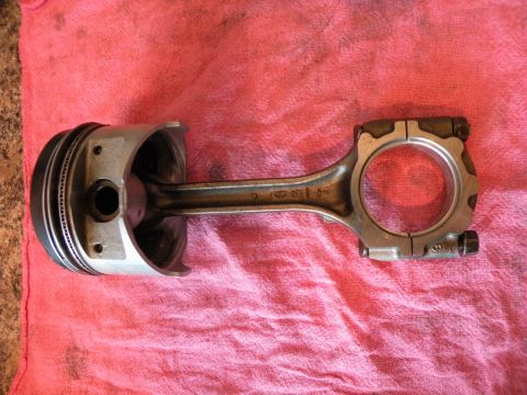 1998 Subaru Legacy - A disassembled engine component, a piston connected to its rod, rests on a pink fabric surface.