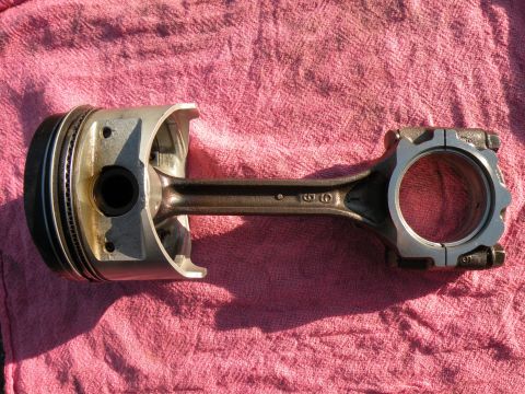 1998 Subaru Legacy - A piston and connecting rod assembly lies on a pink textured cloth.