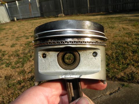 1998 Subaru Legacy - A close-up view of a single engine piston, held in a person's hand against an outdoor backdrop.