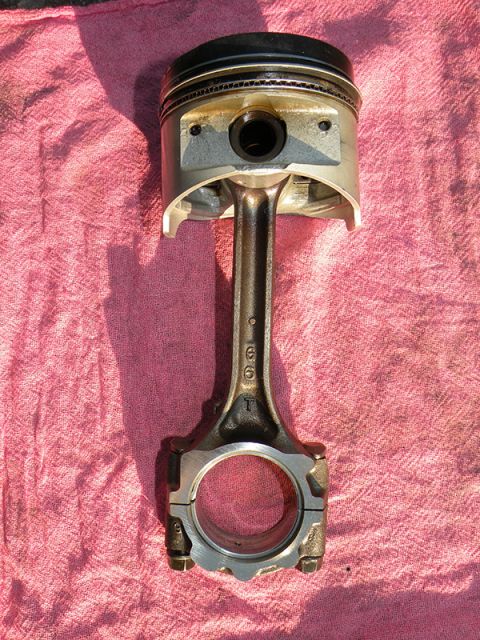 1998 Subaru Legacy - A piston and connecting rod assembly, likely from an engine, is displayed on a pink cloth. Numbers are visible on the connecting rod.