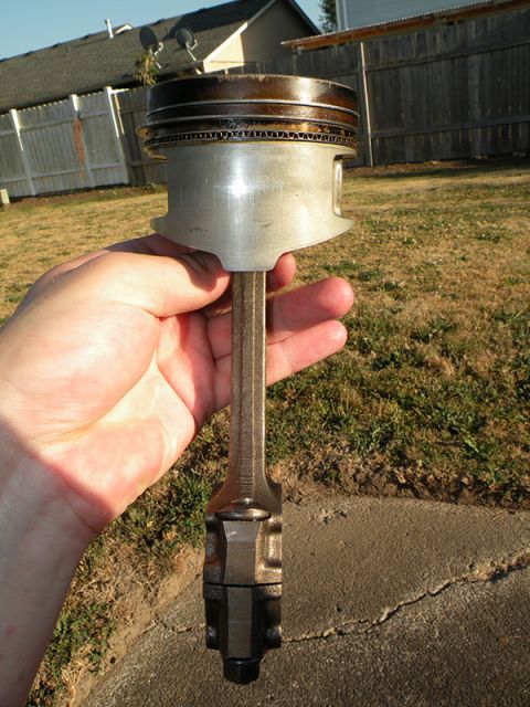 1998 Subaru Legacy - A used engine piston and connecting rod assembly is displayed outdoors.