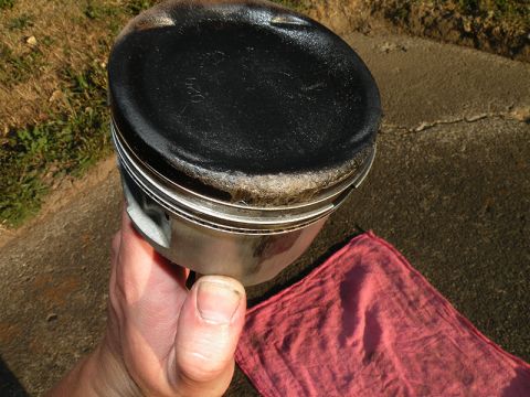 1998 Subaru Legacy - A piston, likely from an engine, shows significant carbon deposits on its crown.