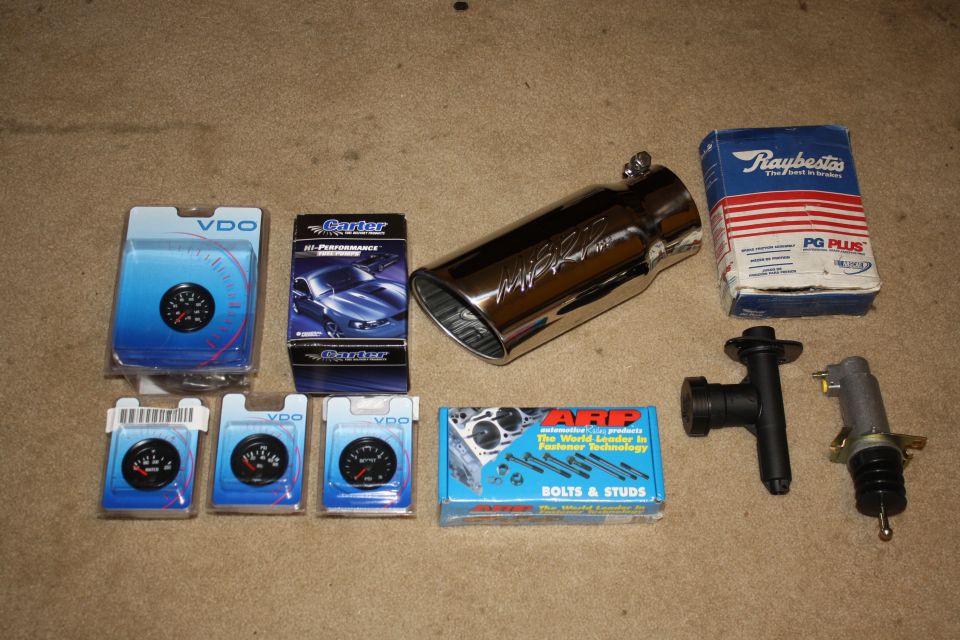 Assortment of automotive parts: VDO gauges, Ganter box, chrome exhaust tip, Raybestos brake box, ARP bolts, and clutch components