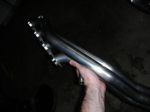 1992 Ford Crown Victoria - Polished metal exhaust headers are held by a hand, showing their intricate pipework and flanged connection.
