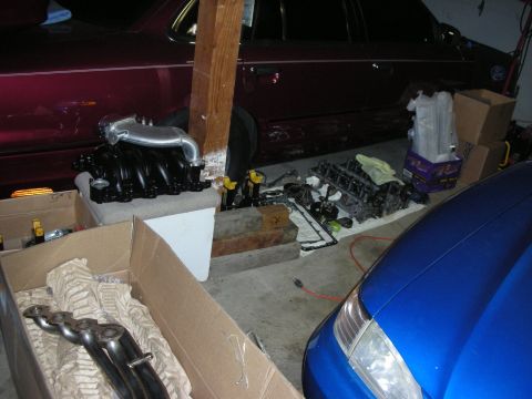 1992 Ford Crown Victoria - Engine components and parts are laid out in a garage, with two vehicles partially visible in the background.