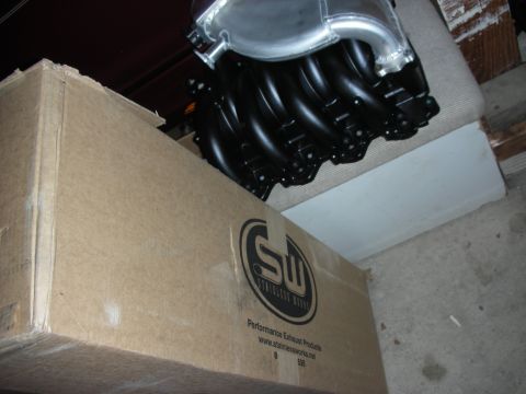 1992 Ford Crown Victoria - A cardboard box with performance exhaust product branding sits next to a black engine manifold with a silver intake.