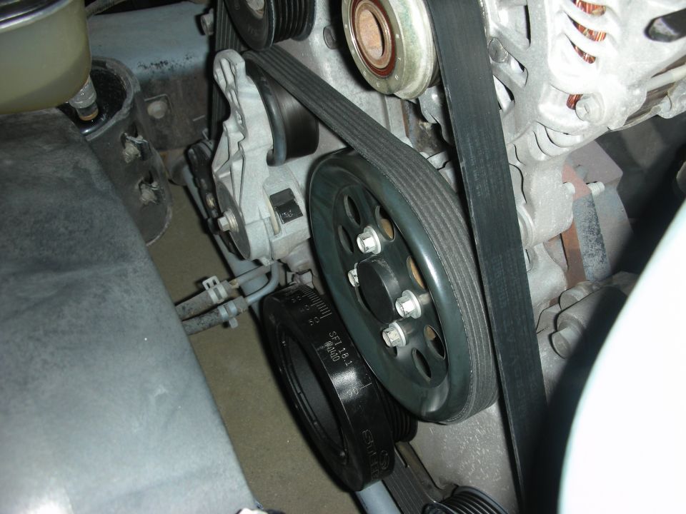 Close-up of black crank pulley, serpentine belt and alternator in an engine bay