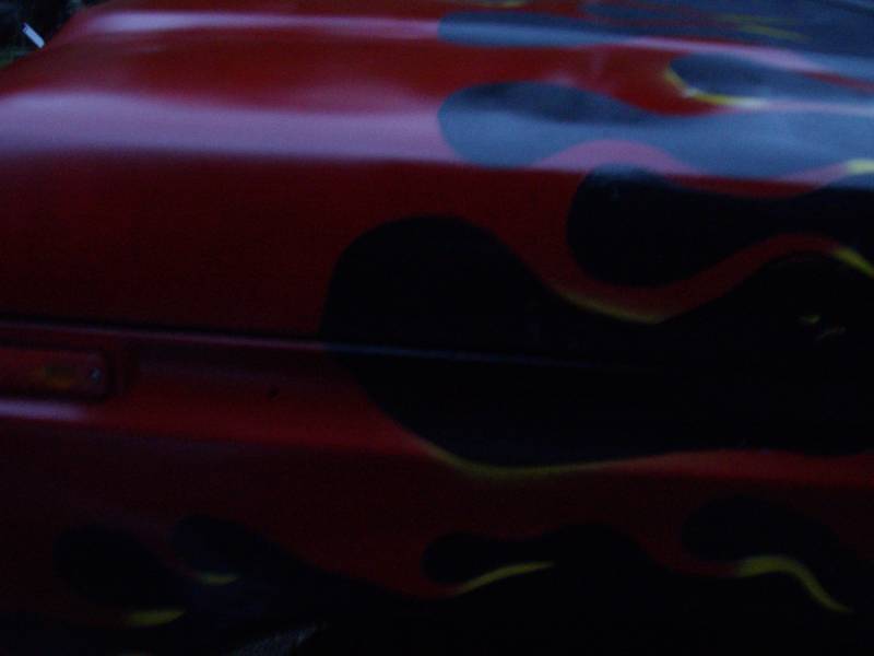 Close-up of a red fender and hood seam with black and yellow flame paint and amber marker light