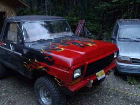 1978 Ford Bronco - Three-quarter front view of a lifted late-1970s Ford 4x4 with a red hood and front clip, black body and orange-and-yellow flame graphics ru…