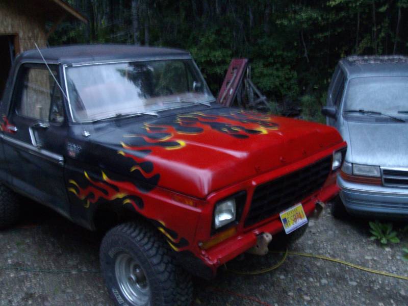 Lifted black-and-red 1970s Ford 4x4 with flame graphics and black soft top on gravel