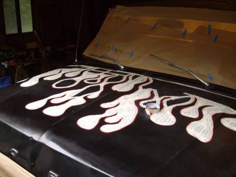 1978 Ford Bronco - A black truck hood masked for a flame paint job in a dim garage, with red fine-line tape outlining the licks and white masking paper filled…