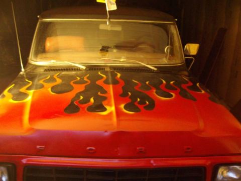 1978 Ford Bronco - Front view over the hood of a red Ford truck painted with black and orange-yellow flame graphics running back toward the windshield. Raised…