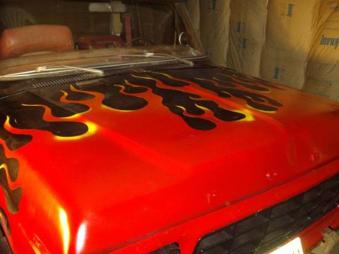 1978 Ford Bronco - Angled close-up of a red truck hood freshly sprayed with black flames outlined in yellow-orange, with the masking removed and the cowl vent…