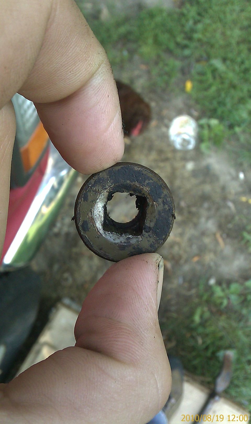 Rubber grommet with square hole held by fingers. Chrome trim visible to the left