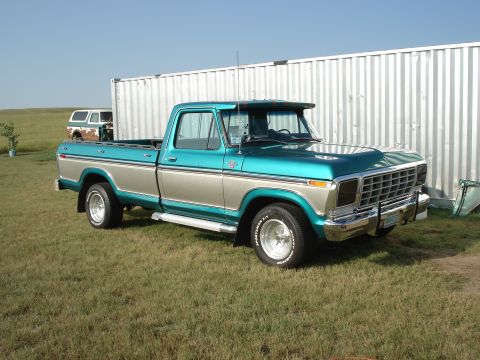 1979 Ford F-150 - A teal and tan 1979 Ford F-150 pickup truck is parked in front of a corrugated metal wall, with another vehicle visible in the background.