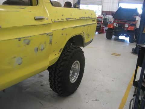 1978 Ford Bronco - Yellow 1978 Ford Bronco in a garage, showing bodywork and large off-road tires. Another vehicle is visible in the background.