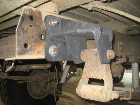 1978 Ford Bronco - Close-up view of the underside of a vehicle, focusing on the frame and suspension system with a jack stand providing support.