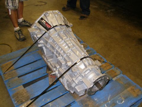 1990 Ford Bronco - A freshly rebuilt aluminum-case automatic transmission strapped to a blue wooden shipping pallet on a shop floor, tail housing and splined…