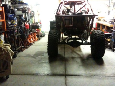 Suzuki Samurai - The rear axle and large tires of a custom off-road vehicle are visible in a cluttered garage setting.