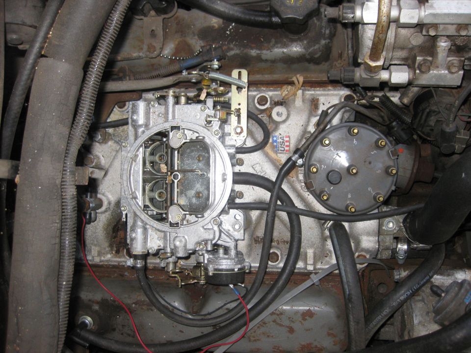 Close-up of an engine carburetor and fuel pump with hoses and wiring