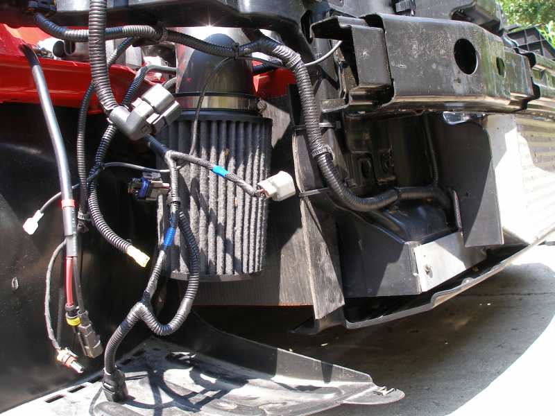 Cone air filter behind a black baffle in the front corner of a car with bumper removed