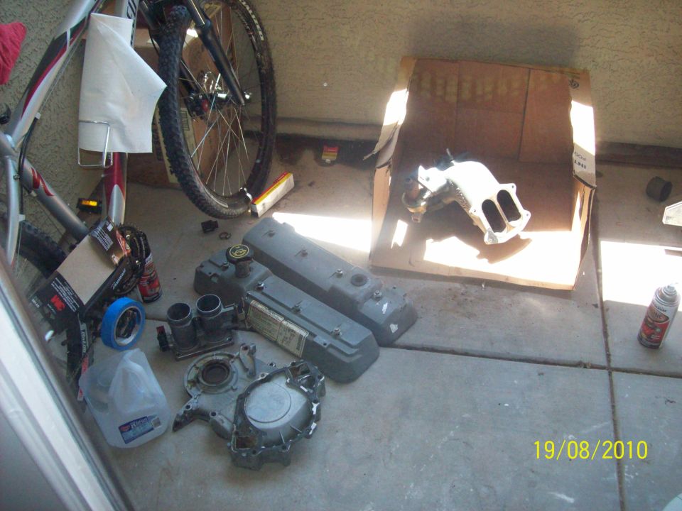 Engine parts, including valve covers and an intake manifold, are laid out on the ground next to a bicycle