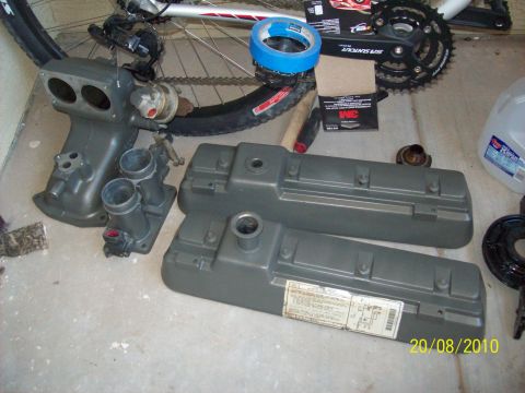 1985 Ford Bronco - Engine parts, including an intake manifold and valve covers, are laid out on a concrete surface next to a bicycle wheel.