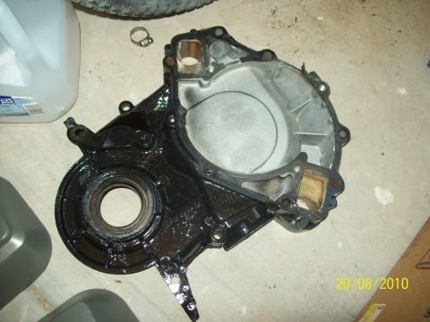 1985 Ford Bronco - An engine timing cover is shown on a concrete surface, with some oil visible.