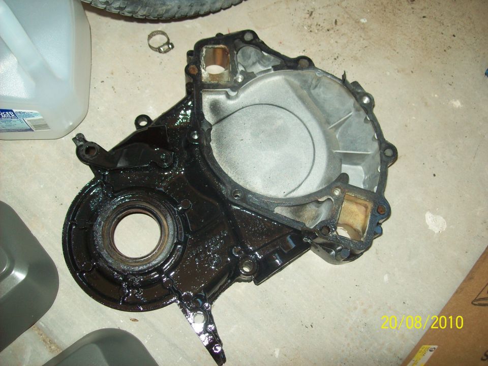 Engine timing cover with oil residue, lying on a concrete floor