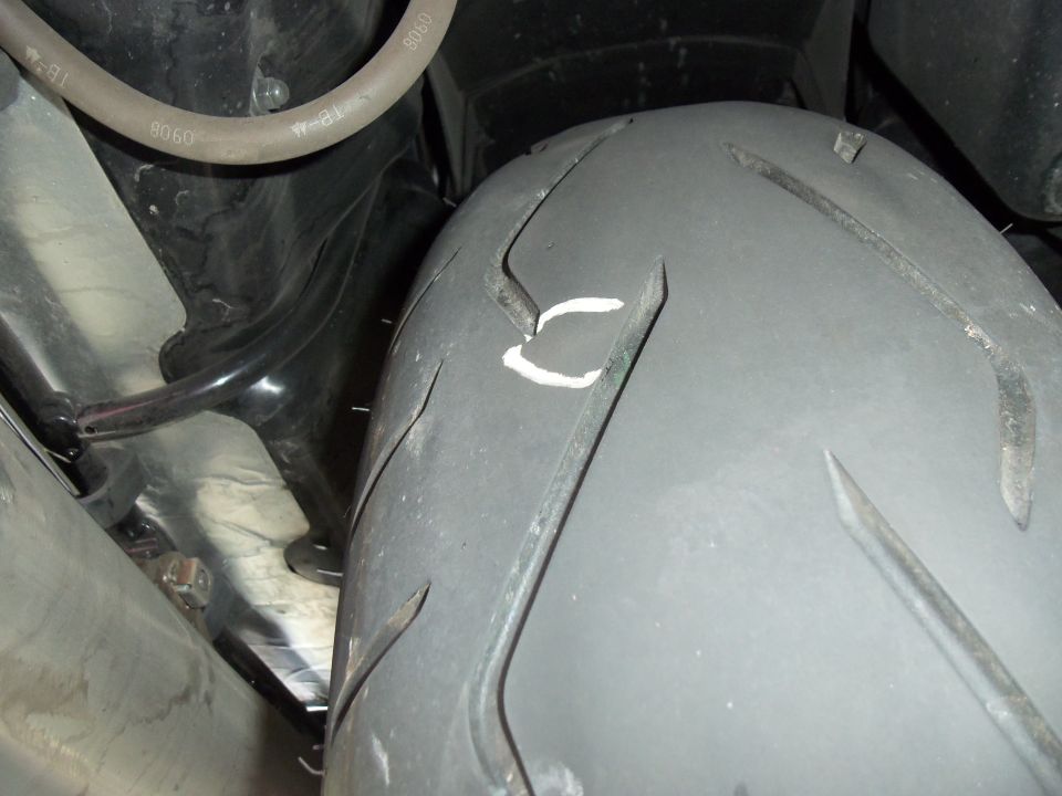 Motorcycle rear tire tread with a white mark, chrome exhaust and hose alongside