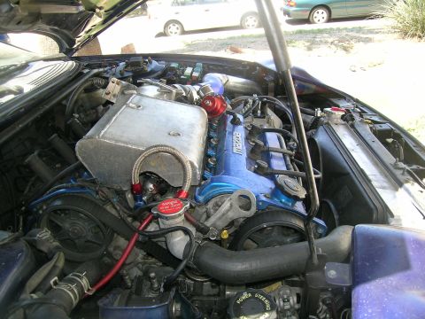 1995 Ford Probe - Customized engine bay a turbo setup and aftermarket intercooler. Other vehicles are parked in the background.