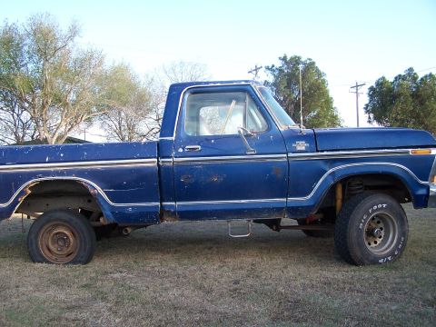 1979 Ford F-150 - This blue 1979 Ford F-150 pickup truck is seen from the side, showing its flat rear tire and weathered paint.