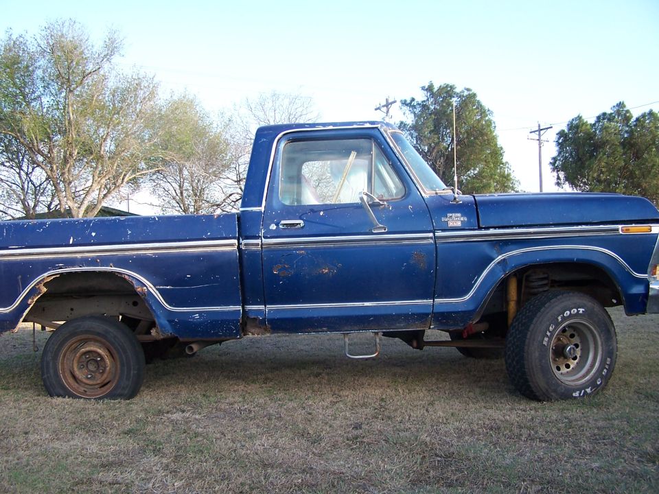 Side view of a blue 1979 Ford F-150 pickup truck with a flat tire