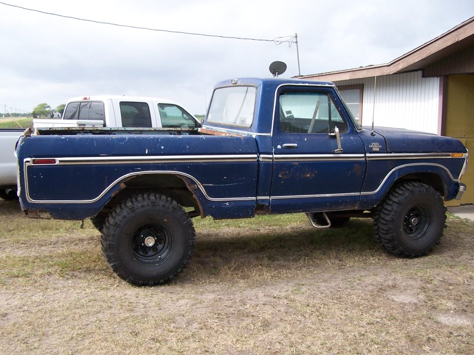 Side view of a lifted blue 1979 Ford F-150 pickup truck parked next to a white pickup truck