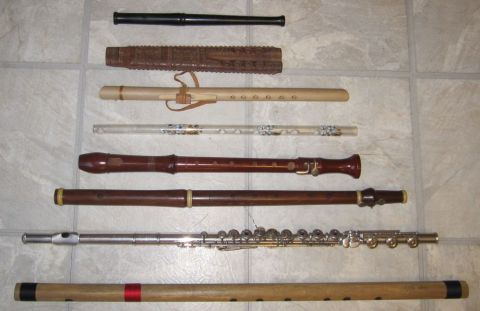 1990 Ford Bronco - Eight woodwind instruments laid out in rows on a tile floor, including a black plastic fife, a carved wooden flute, a Native American-style…