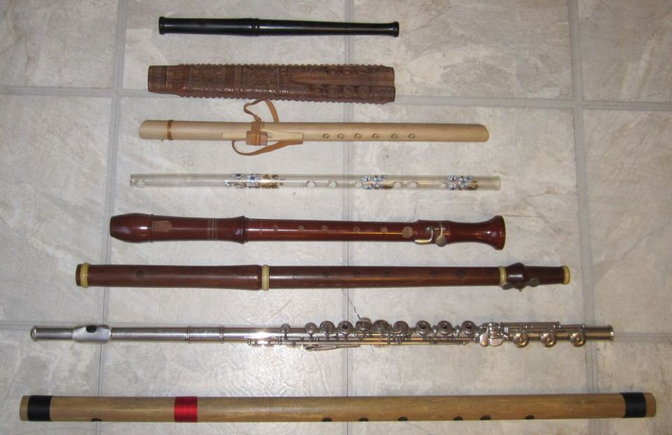 Eight flutes and recorders of wood, metal and acrylic laid out on a tile floor
