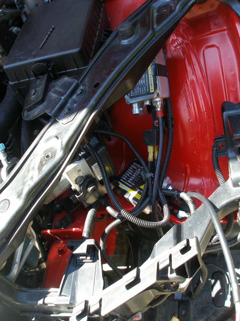 HID ballasts and wiring loom mounted in the corner of a red car's engine bay