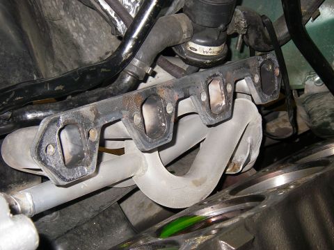 1990 Ford Bronco - Close-up of an engine's exhaust header bolted to the cylinder head, with ceramic-coated white tubular primaries curving down and a Ford-sta…