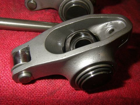 1990 Ford Bronco - Close-up of a polished stainless steel full-roller rocker arm showing its roller trunnion bearing and pushrod cup, with a second rocker and…